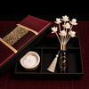 A luxury Thai Neroli  diffuser gift set by CHAYIN, featuring a black glass bottle with a  tassel, white lotus-shaped reeds, a small cream-colored ceramic bowl, and a red presentation box with a gold patterned band. 